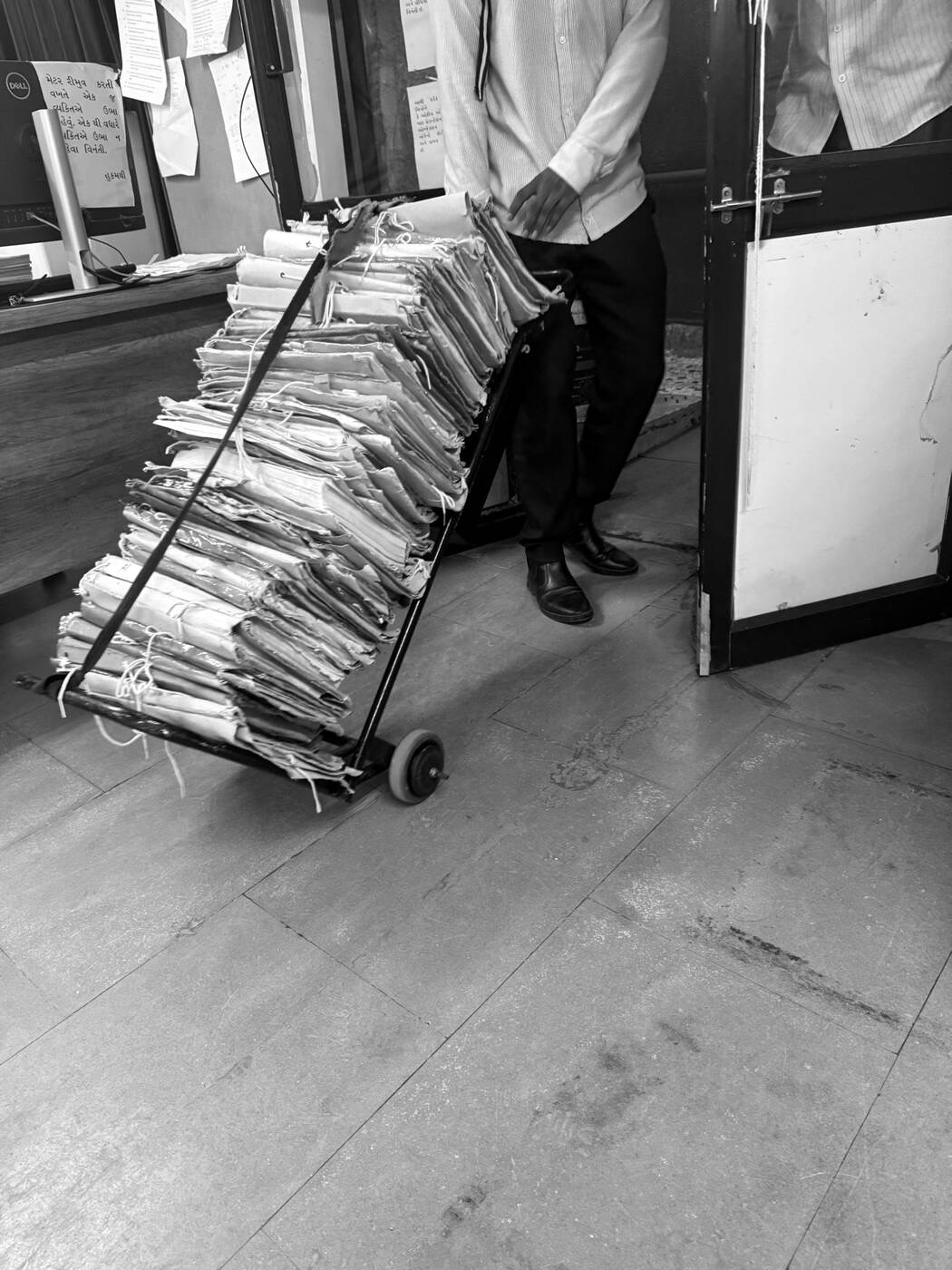 A registry clerk wheeling a trolley stacked with tied paper case files.