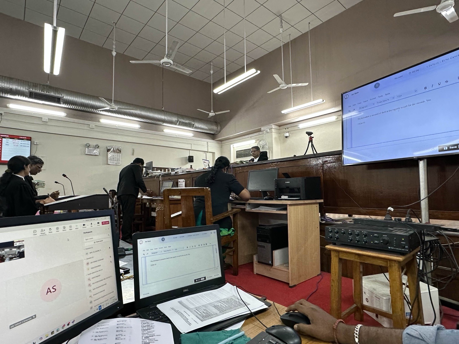A courtroom at the High Court of Judicature at Madras, with jhana's live dictation on screen beside the bench.